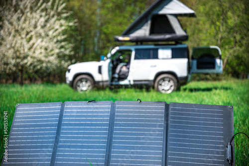 4x4 Offroad vehicle camping with roof tent in a meadwow with solar panel for energy generation in foreground