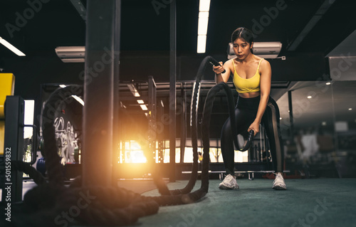 Battle ropes session. Attractive young fit and toned Asian sportswoman working out in functional training gym doing crossfit exercise with battle ropes.