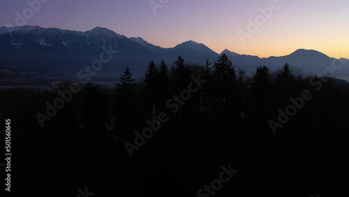 Bled Lake and Marijinega Vnebovzetja Church in Morning Twilight. Blue Hour. Hills and Forest. Julian Alps. Slovenia, Europe. Aerial View. Drone Flies Forward over Trees at Low Level. Reveal Shot photo