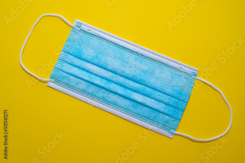 Blue surgical mask, on a yellow surface. Obligation to wear a mask. 