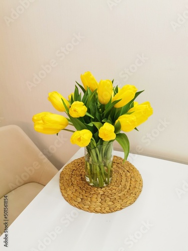 Yellow spring tulips on a white table on a wicker placemat. Minimalist composition with flowers.