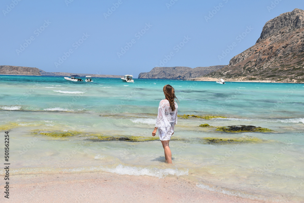 Pretty blonde girl in white beach dress stands facing turquoise blue Mediterranean sea on a hot summer day in Greece Pretty blonde girl in white beach dress stands facing turquoise blue Mediterranean sea on a hot summer day in Greece