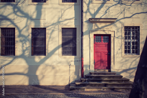 facade of an old building with a red door shadow from a tree © luchschenF