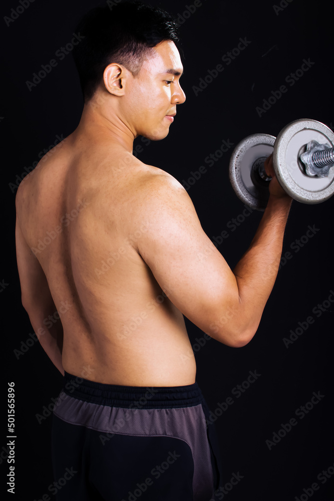 Portrait of handsome asian young muscular man, smiling, standing and lifiting dumbbell on isolated black background cutout. Sport and Healthy Concept.