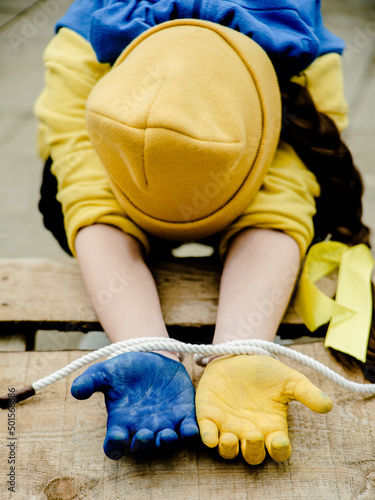 A child with his hands tied and in the yellow and blue color of the Ukrainian flag. Russia's invasion of Ukraine, a request for help to the world community. Children ask for peace. Stop the war.