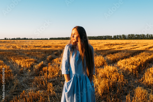 Escapism, getting away from it all, mental health, Stress resilience. Alone Young woman in linen dress walking on mowed wheat field at sunset. Peaceful woman with long hair spending time in nature #501569058