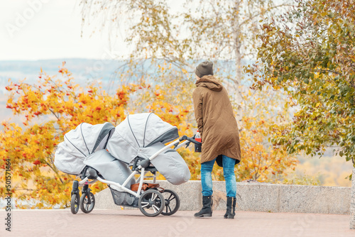 Mother woman walks with twin baby stroller or pushchair in autumn park photo