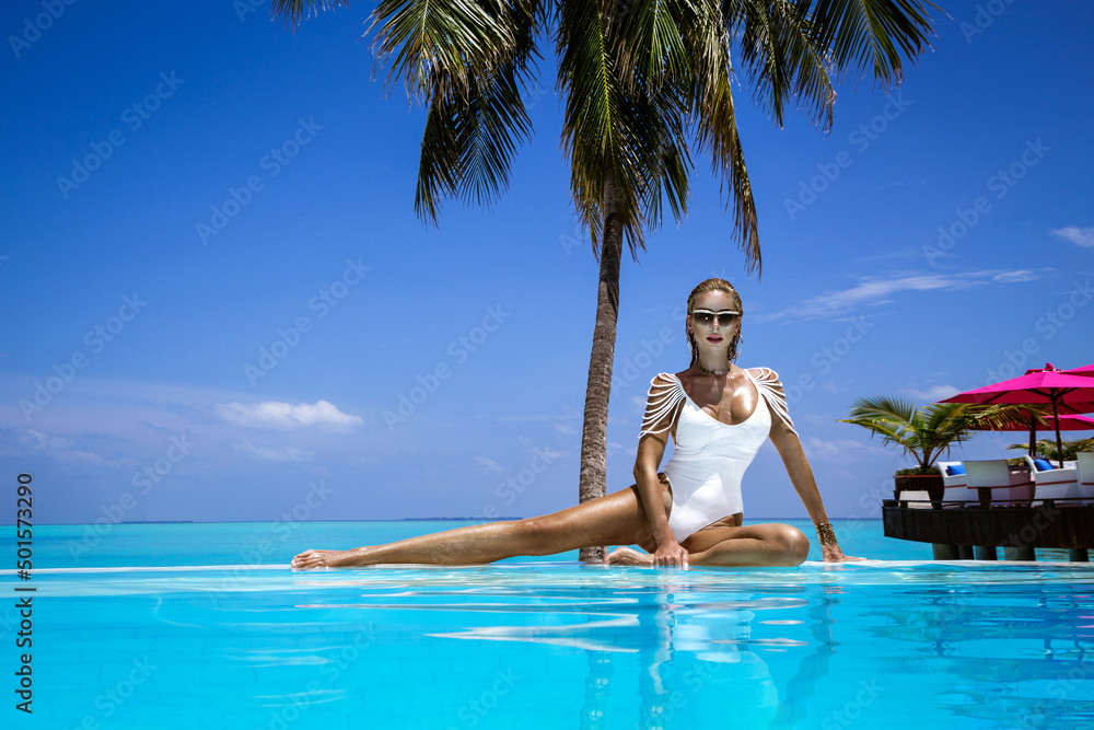 Elegant tanned woman in white swimsuit in pool on tropical Maldives