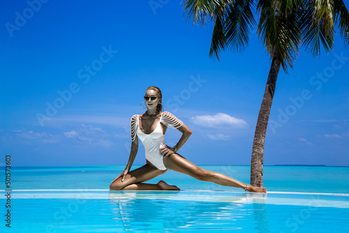 Elegant tanned woman in white swimsuit in pool on tropical Maldives island. Beautiful bikini body girl in pool with view on horizon. Sexy model near the pool on beautiful Indian ocean landscape.Travel