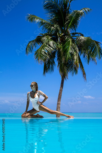 Elegant tanned woman in white swimsuit in pool on tropical Maldives island. Beautiful bikini body girl in pool with view on horizon. Sexy model near the pool on beautiful Indian ocean landscape.Travel