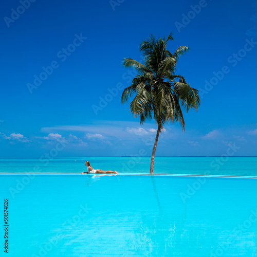 Fototapeta Naklejka Na Ścianę i Meble -  Elegant tanned woman in white swimsuit in pool on tropical Maldives island. Beautiful bikini body girl in pool with view on horizon. Sexy model near the pool on beautiful Indian ocean landscape.Travel
