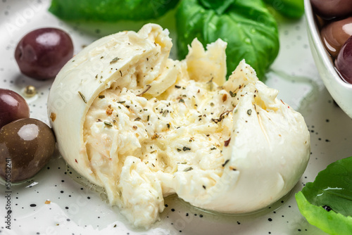 Creamy Italian Burrata Cheese with basil and olive oil on white plate. Italian Mediterranean cuisine. Food recipe background. Close up