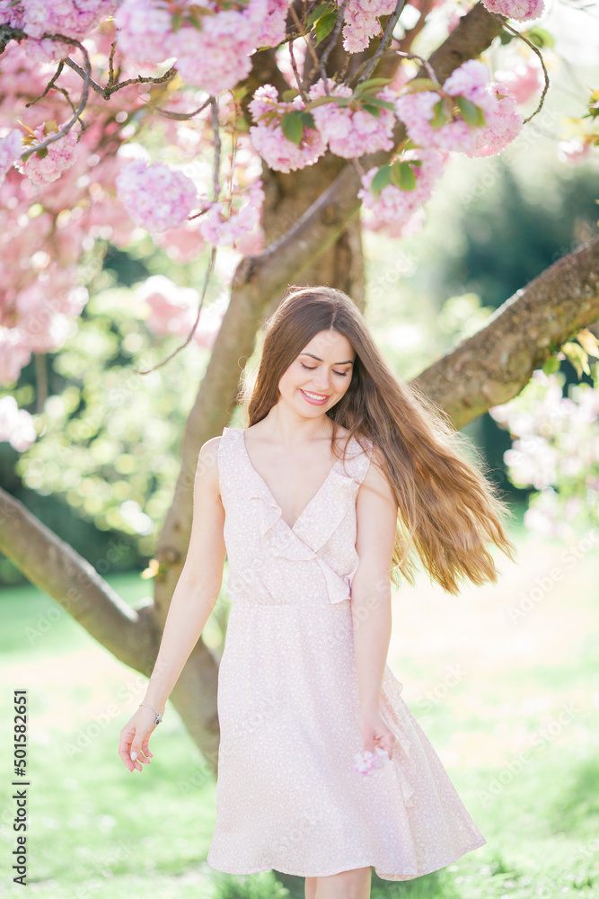 Spring portrait of a young beautiful woman in pink blossoms. Young beautiful model with long hair, in a wicker hat and a light dress near the cherry blossoms. Spring portrait of a young beautiful woman in pink blossoms. Young beautiful model with long hair, in a wicker hat and a light dress near the cherry blossoms.