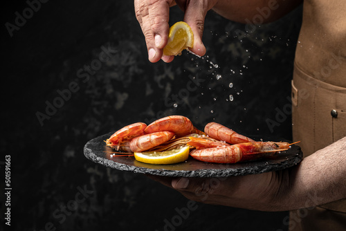 chef is cooking delicious shrimp with seasoning, Prawns fried with splashes of lemon juice in a freeze motion on a dark background. Seafood appetizer. Culinary, cooking concept