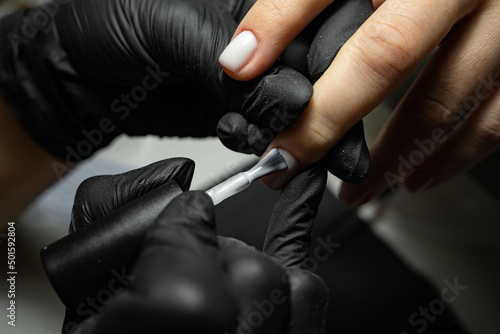 the process of applying varnish on nails in a beauty salon close-up. A woman in the salon receives a manicure from a beautician. Transparent nail polish and brush, macro.