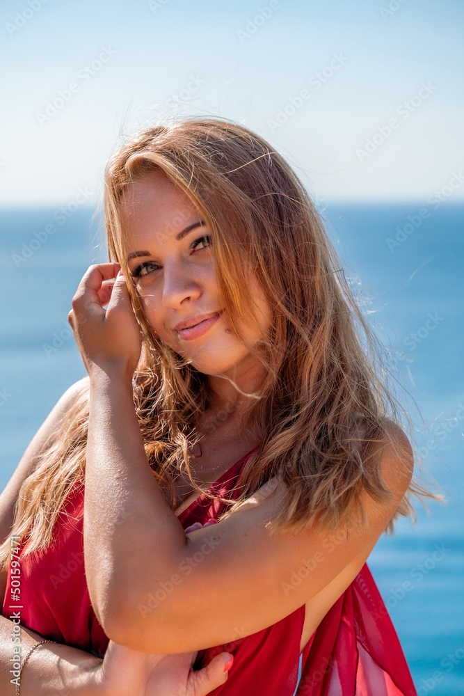 Smiling young woman in a red dress looks at the camera. A beautiful tanned girl enjoys her summer holidays at the sea. Portrait of a stylish carefree woman laughing at the ocean. Smiling young woman in a red dress looks at the camera. A beautiful tanned girl enjoys her summer holidays at the sea. Portrait of a stylish carefree woman laughing at the ocean.
