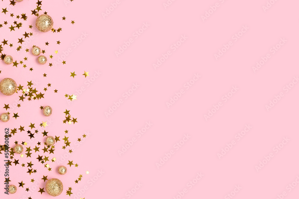 Various gold colored glittering confetti on a pink pastel background with copy space.