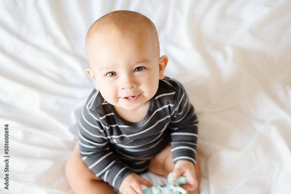 little boy 6 months old sits on a white blanket and smiles little boy 6 months old sits on a white blanket and smiles