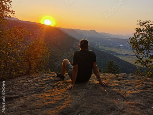 A young man is sitting on a cliff during the sunset.