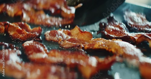 Closeup slider shot of fresh bacon being flipped on a griddle. 4K cinematic footage.