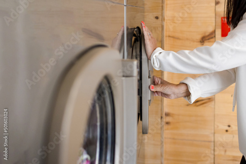 Woman closing the door of a washing machine in an industrial self-service laundromat