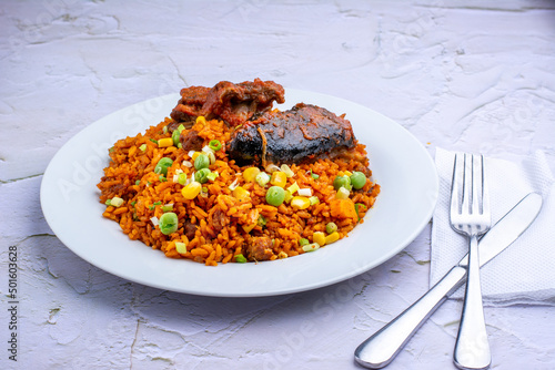 Jollof Rice and vegetables with stewed Goat meat in a white ceramic plate on an embossed background