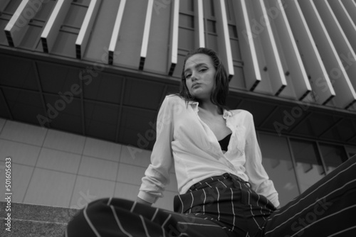 A young brunette girl in white shirt and striped trouser is sitting on the stairs