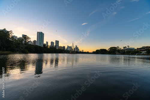 Igapo lake at sunset, Londrina - PR, Brazil. Beautiful city lake surrounded by trees, with calm water and the city buildings on background. photo