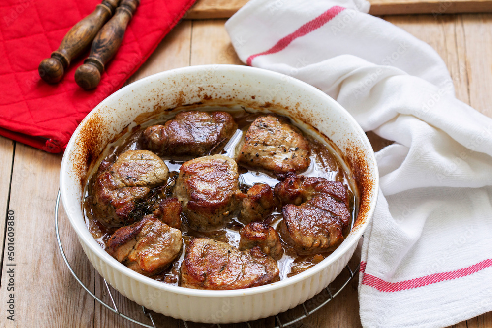 Tenderloin baked in onion sauce with herbs on a wooden table. Rustic style.
