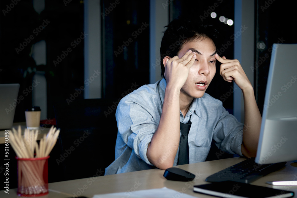 Asian young tired staff officer man using desktop computer having overwork project overnight in office, exhausted unhappy businessman feeling sleepy after after working hard overtime at night. Asian young tired staff officer man using desktop computer having overwork project overnight in office, exhausted unhappy businessman feeling sleepy after after working hard overtime at night.