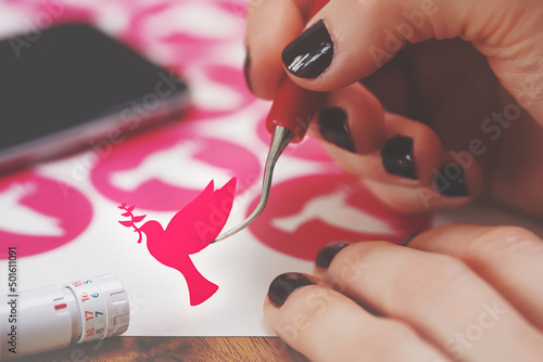 women hands with painted nails hold freshly cut peace dove decal that sticks to tip of curved weeding tool. pink adhesive film. wooden worktop. adjustable plotting blade in foreground. selective focus