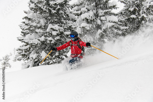Woman skier in bright ski suit, helmet and goggles sliding down snow-covered slopes on skis