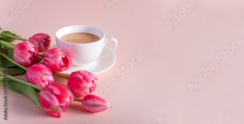 Banner.One cup of hot, morning coffee and a bouquet of pink-lilac tulips on a bright pink background. View from above.Copy space for text. The concept of holidays.