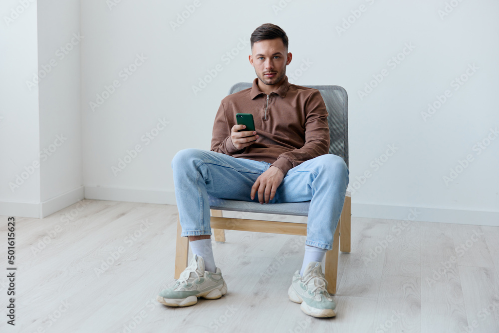 Happy young man holds phone chatting with girlfriend sitting at chair in office looks at camera on over white wall home background. Social Media concept. Copy space for ad. Mobile App offer Banner