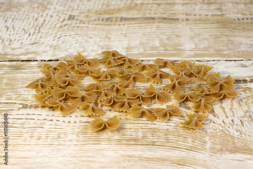 Whole grain dark pasta bows on brown plate on a rough wooden light background with selected focus