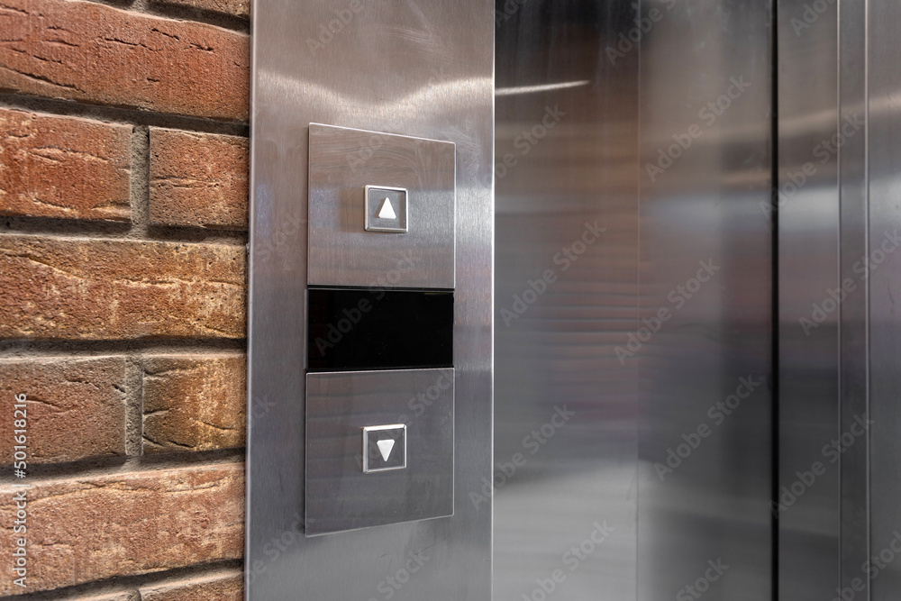 Two elevator call buttons up and down on a metal panel with a red brick wall
Two elevator call buttons up and down on a metal panel with a red brick wall