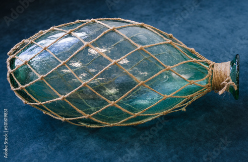 On  blue background is  large glass bottle covered with  woven net of coarse rope.