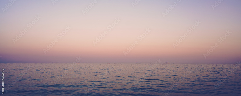 Beautiful panoramic view to calm sea surface with cargo tanks on horizon line at sunset