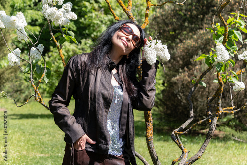 A happy girl with long black hair in glasses holds a white lilac branch in her hands in the garden. Rest in the park.