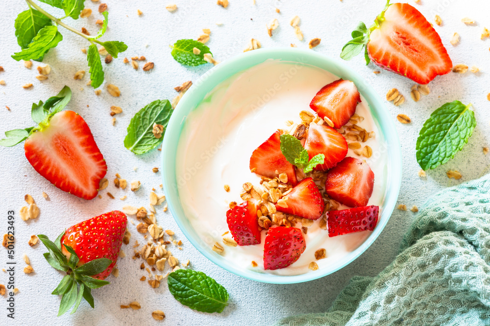 Yogurt with granola and strawberry in blue bowl at light stone table. Top view. Yogurt with granola and strawberry in blue bowl at light stone table. Top view.