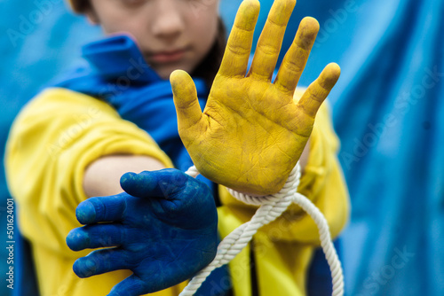 girl with a braid in a yellow sweater on a blue background with tied hands painted in blue and yellow Ukrainian flag