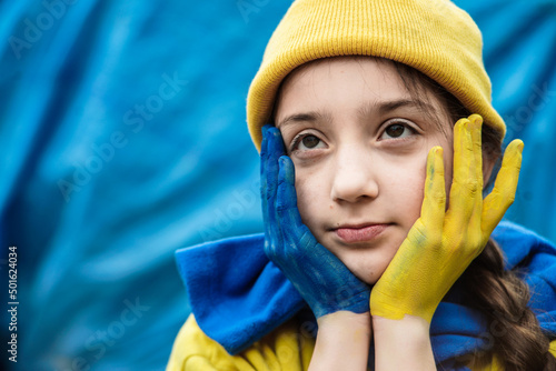 girl with a braid in a yellow sweater on a blue background with a hand painted in blue and yellow Ukrainian flag. Children ask for peace. Stop war