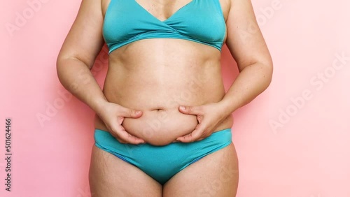 Cropped shot of overweight fat woman holding tummy flabs with obesity, excess fat in blue swimsuit. Go on unhealthy diet. Emphasizing by hands excess adiposity. Overeating problem, obesity.  photo