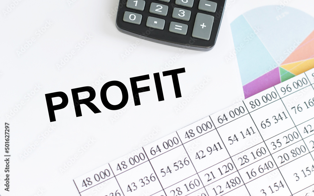 PROFIT text on a notepad on a table next to charts, reports and a calculator PROFIT text on a notepad on a table next to charts, reports and a calculator
