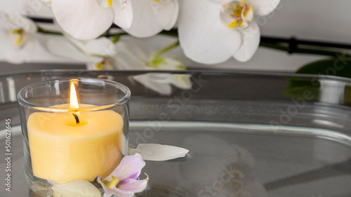 Still life on a background of white orchids and a candle in the water and burning yellow flame
