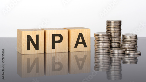 npa - text on wooden cubes on a cold grey light background with stacks coins photo