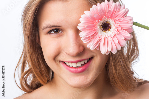 Portrait of a happy girl with fresh skin holding a flower over one eye on white background. Close up portrait of beautiful redhead curly woman pnik flower wearing white tshirt. Beauty and spring photo
