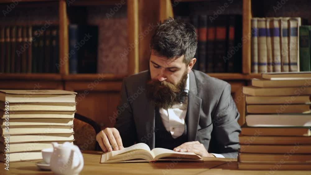 Man reading book in classical library cabinet. Home library. Businessman sits in vintage interior, holds book. Business man in suit in his cabinet. Mature man with calm face enjoys reading. Man reading book in classical library cabinet. Home library. Businessman sits in vintage interior, holds book. Business man in suit in his cabinet. Mature man with calm face enjoys reading.