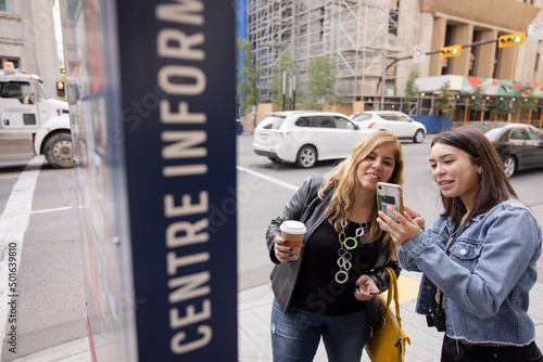 Mother and daughter with smart phone at information board in city