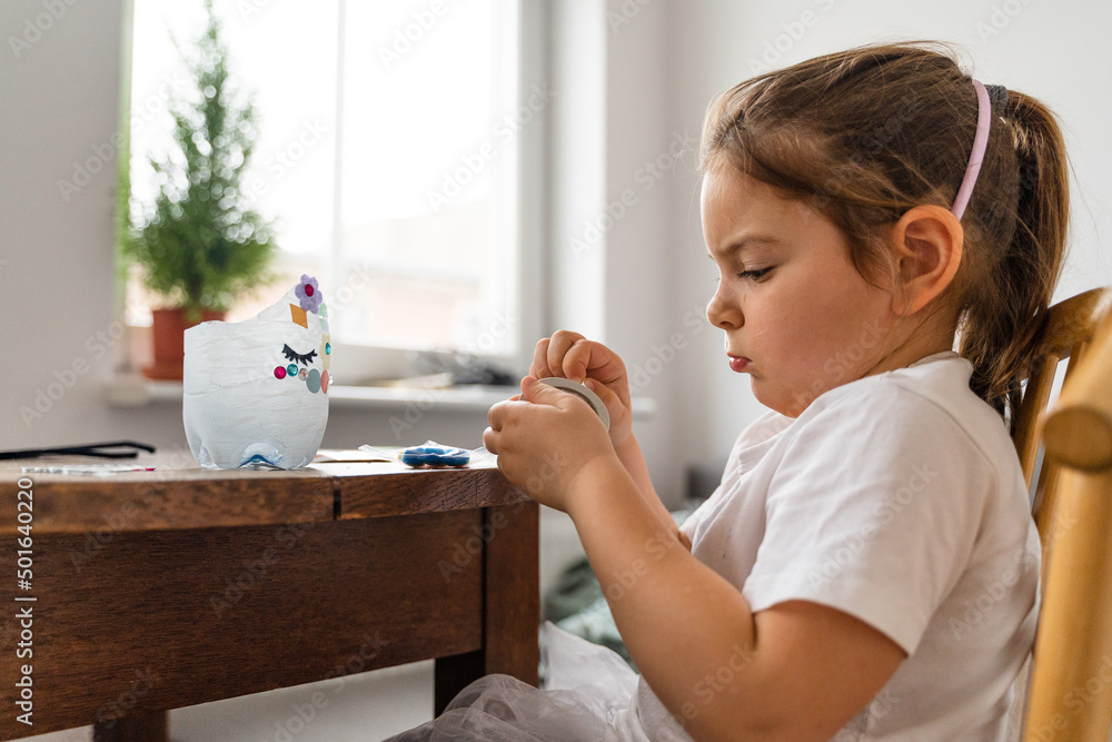 Beautiful caucasian preschool girl playing at home and doing crafts from plastic bottle. Recycle toys and diy creativity Beautiful caucasian preschool girl playing at home and doing crafts from plastic bottle. Recycle toys and diy creativity
